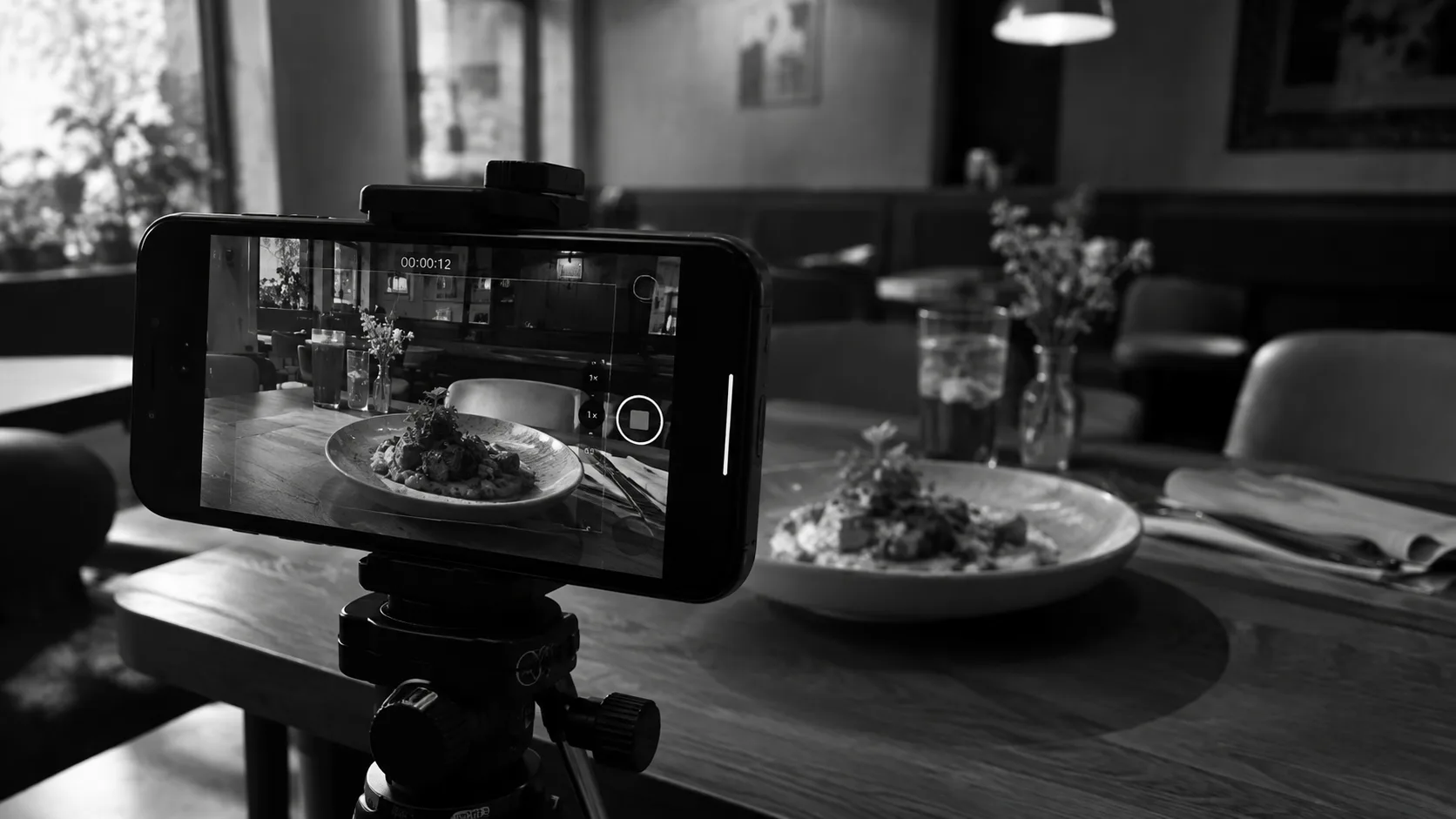 Smartphone auf einem Stativ filmt einen Teller in einem Restaurant, Schwarzweiß